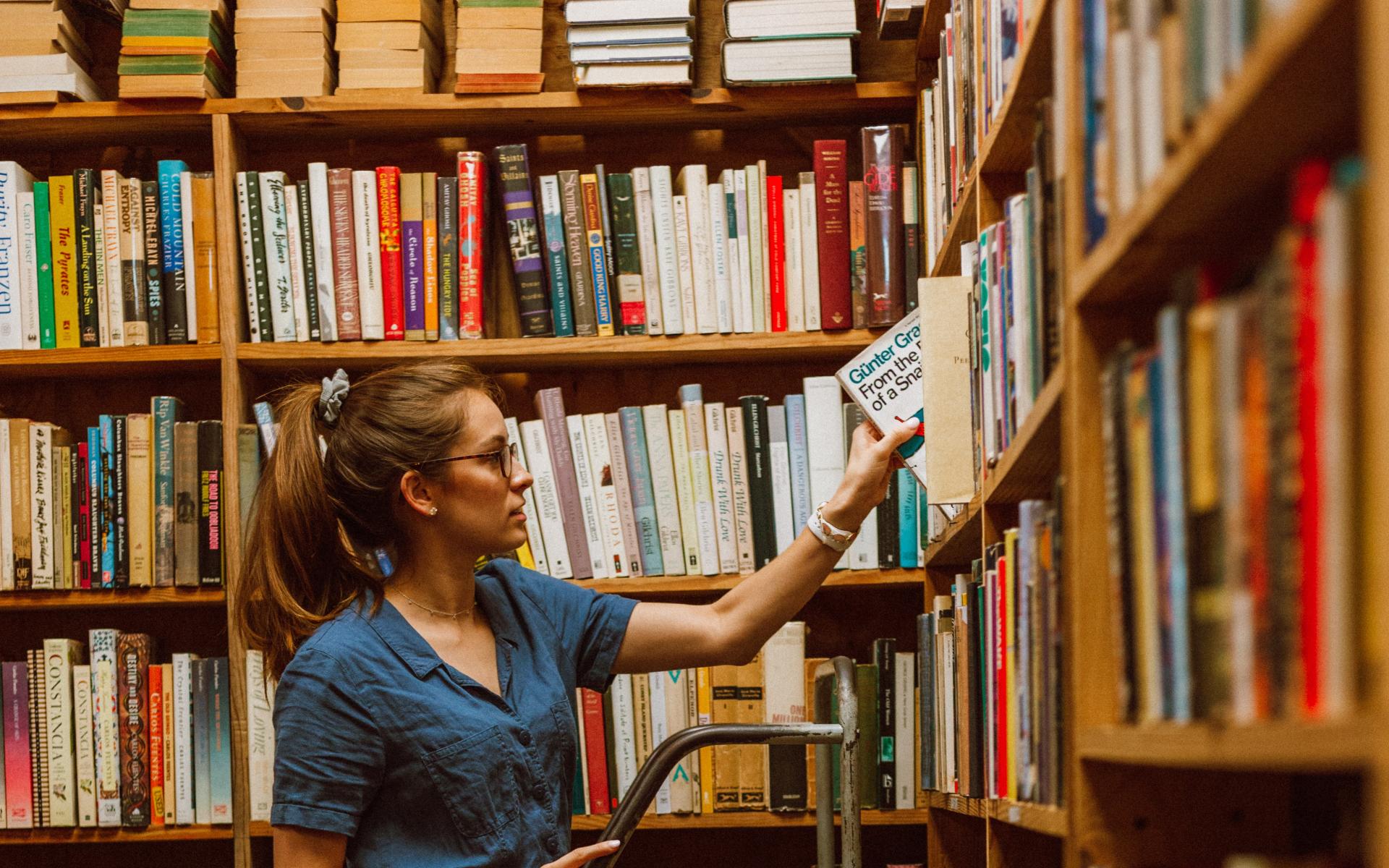 Junge Frau auf einer Leiter vor dem Bücherregal